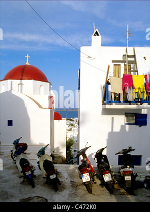 Servizio lavanderia si blocca sul portico sopra parcheggiato scooters nella città vecchia di Mykonos in Grecia Foto Stock