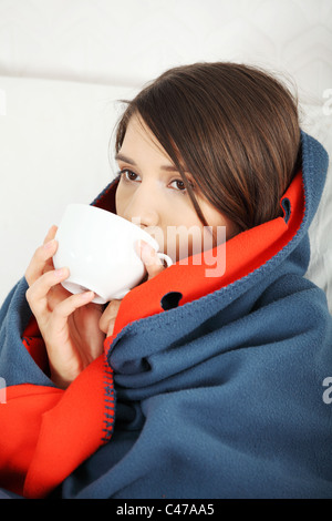 Giovane donna sorpresa freddo, avvolto in una coperta, bere qualcosa di caldo da cup. Foto Stock