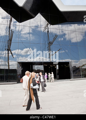 I visitatori al di fuori del Riverside Museum di Glasgow. I montanti del Glenlee (Tall Ship) sono riflesse nella parete di vetro. Foto Stock