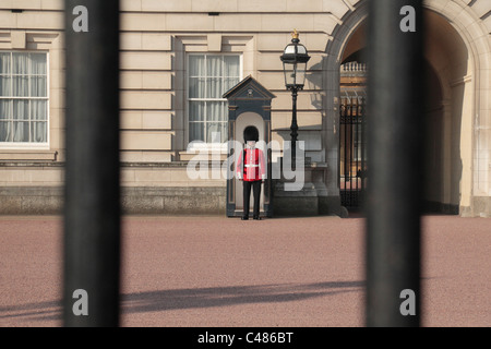 Una vista attraverso le ringhiere fuori Buckingham Palace, London, Regno Unito. di un soldato della regina della guardia di turno. Foto Stock