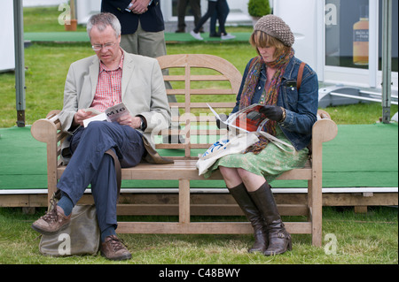 L uomo e la donna la lettura di libri e riviste seduto sulla panca di legno a Hay Festival 2011 Foto Stock