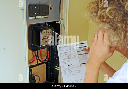 Donna contemplando l'aumento dei prezzi dell'energia e delle fatture nel Regno Unito come lei legge il suo contatore elettrico Foto Stock