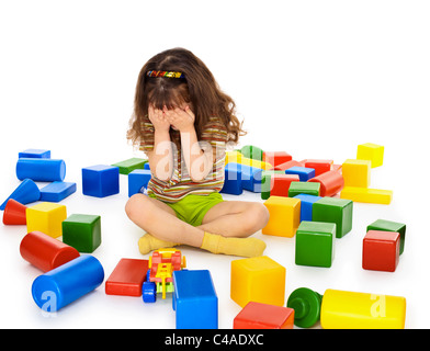 Una bambina seduta su uno sfondo bianco tra i giocattoli e pianto Foto Stock