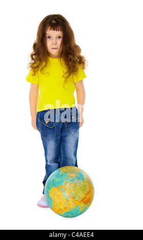 Funny little girl in jeans con un globo geografico come un pallone da calcio isolati su sfondo bianco Foto Stock