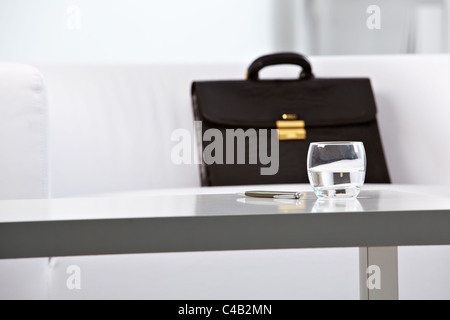 Close-up del posto di lavoro in un ufficio con un bicchiere di acqua, penna e valigetta ventiquattrore su sfondo Foto Stock