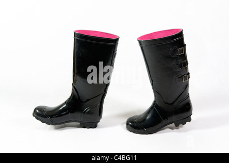 Una coppia di wellies nero o stivali in gomma con rosa all'interno adottate contro uno sfondo bianco posizionato come se essi sono a piedi Foto Stock