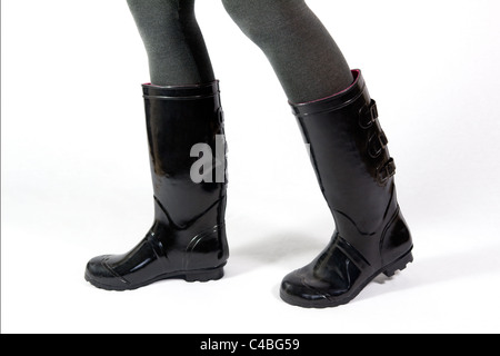 Al di sotto del ginocchio colpo di una coppia di gambe femminili per camminare in nero wellies o stivali in gomma presi contro uno sfondo bianco Foto Stock