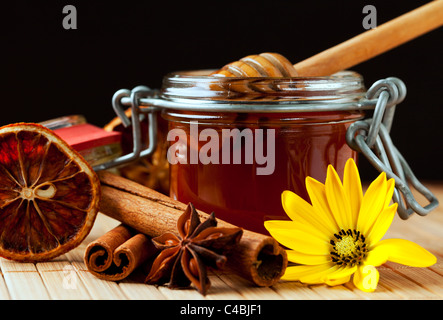 Miele aromatico in un vasetto di miele drizzler, bastoncini di cannella, anice stellato, essiccato fetta di arancia, fiore giallo Foto Stock