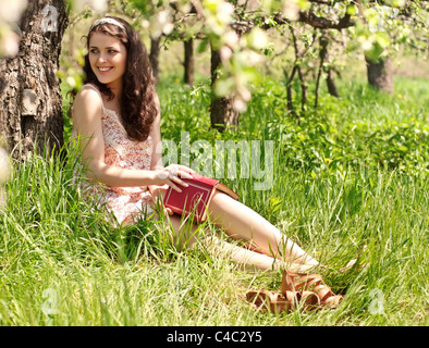 Ragazza giovane con un libro seduti sotto un albero Foto Stock