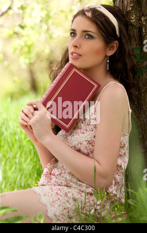 Ragazza giovane la lettura di un libro sotto il melo. Ella è sognare Foto Stock