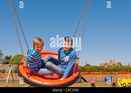 Due ragazzi su uno swing presso il parco giochi in Westleton , Suffolk , Inghilterra , Inghilterra , Regno Unito Foto Stock