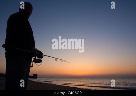 Un pescatore la pesca con lenza in mare mentre il sole tramonta sulla costa a Marget, Kent Foto Stock