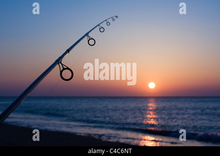 Un pescatore la pesca con lenza in mare mentre il sole tramonta sulla costa a Marget, Kent Foto Stock