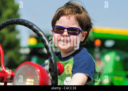 Little Boy sorrisi come egli gode di un immaginario giro su un trattore sul visualizzatore in corrispondenza di una farm locale ufficio di presidenza toccare un evento del trattore. San Carlo, Illinois, Stati Uniti d'America. Foto Stock