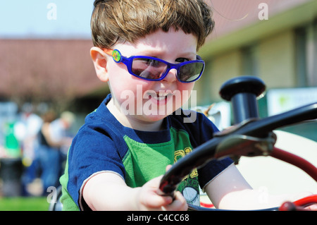 Little Boy sorrisi come egli gode di un immaginario giro su un trattore sul visualizzatore in corrispondenza di una farm locale ufficio di presidenza toccare un evento del trattore. San Carlo, Illinois, Stati Uniti d'America. Foto Stock