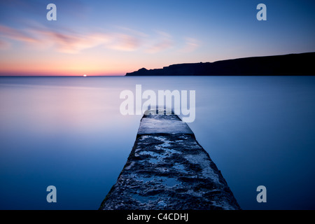 Sunrise fa capolino oltre l'orizzonte a Runswick Bay nei pressi di Whitby con il molo di pietra che conduce attraverso l'immagine Foto Stock