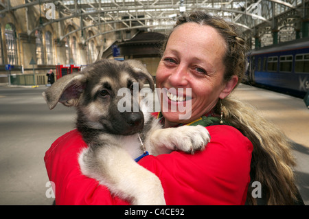 Donna che mantiene il suo cucciolo alsaziano prima di salire a bordo di un treno alla Stazione Centrale di Glasgow, Glasgow, Scotland, Regno Unito Foto Stock