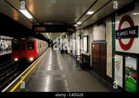 Un treno della District Line arrivando a St James Park stazione della metropolitana di Londra, Inghilterra, Regno Unito Foto Stock