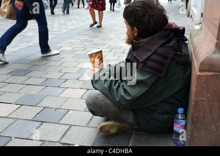 Uomo seduto e a mendicare per Sauchiehall Street, Glasgow, Scozia, mentre la gente ignora lui e a piedi da Foto Stock