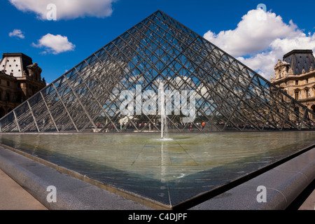 La piramide di vetro e una fontana ingresso al museo del Louvre Parigi Francia bel cielo azzurro sfondo e nuvole dimensionale Foto Stock