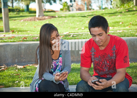 Due California multi etnico razziale etnicamente diversi adolescenti texting utilizzando iPhone Blackfoot American Indian, Ispanico teens telefono mobile device. Signor Foto Stock