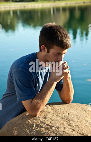16-18 anni di età giovane uomo meditando prega e premurosa da sola nel parco. Natura, ambiente naturale pensieroso dreaming seduta signor © == Foto Stock
