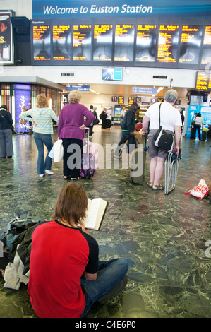 La stazione di Euston. Uomo seduto sul pavimento la lettura in attesa di un treno. Foto Stock