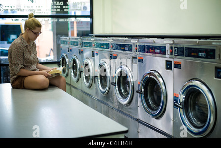 Giovane donna lettura in lavanderia a gettoni Foto Stock