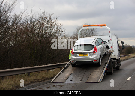 Un argento auto si è rotta e magari è stato un incidente, viene prelevato da un camion di recupero sul lato della strada. Foto Stock