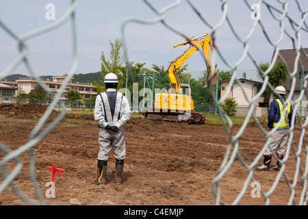 Lavoratori rimuovere la parte superiore del suolo contaminato da radiazioni nucleari, a scuola a Fukushima city, Giappone. Foto Stock