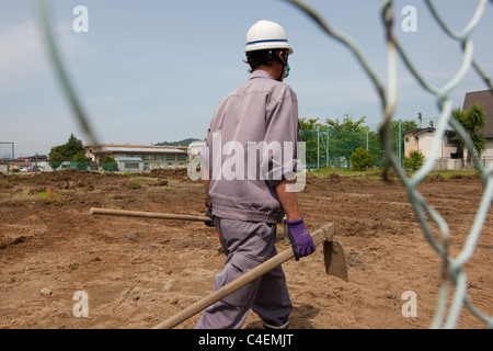 Lavoratori rimuovere la parte superiore del suolo contaminato da radiazioni nucleari, a scuola a Fukushima city, Giappone. Foto Stock