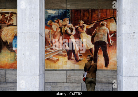 Una donna che guarda la parete socialista murale di felice i lavoratori sulla parete del ministero delle Finanze in edificio ex Berlino Est Foto Stock