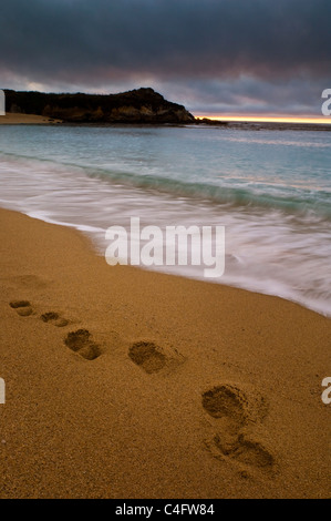 Onde che si infrangono accanto a impronte di sabbia in spiaggia al tramonto, Fiume Carmel membro Beach, California Foto Stock