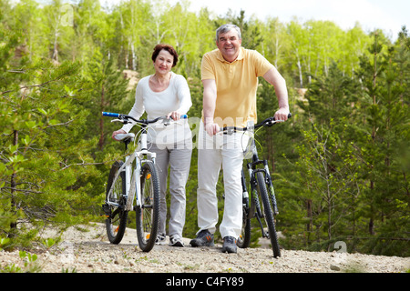 Ritratto di felice coppia matura con biciclette guardando la fotocamera Foto Stock