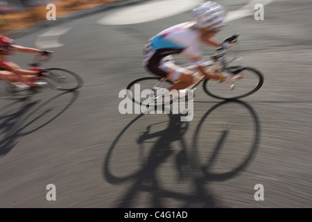 Con la moto di ombre, offuscata donne i ciclisti si trasformano in un angolo di una strada Woking durante l'Halfords 2011 Tour serie. Foto Stock