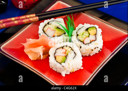 Tre California Sushi rotoli su una targhetta rossa con decorazione verde e nero bastoncini. Foto Stock