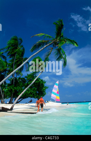 Coppia con il loro catamarano parcheggiato sulla riva sabbiosa in Maldive Foto Stock