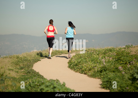 Due femmine atletica, in abiti da allenamento, in esecuzione su un percorso sterrato attraverso la natura nelle ore diurne Foto Stock