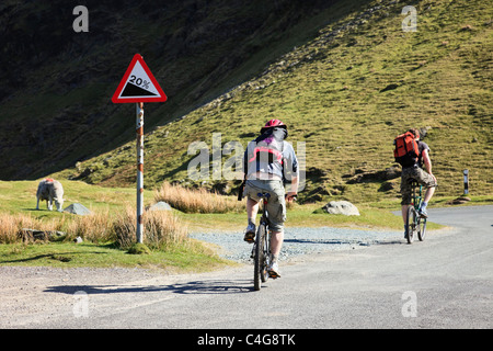 I ciclisti pedalando attraverso un gradiente ripido segno su una strada di montagna attraverso Newlands passano nel Parco Nazionale del Distretto dei Laghi England Regno Unito Foto Stock