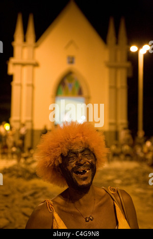 Strada di carnevale partito comunitario noto come Carnavila Reveler indossando il costume di carnevale di fronte della chiesa cattolica Foto Stock