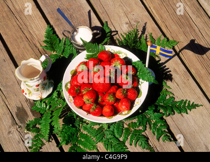 Coppa di fragole con ceramica creamer e zucchero il dock in legno con una piccola bandiera svedese Foto Stock