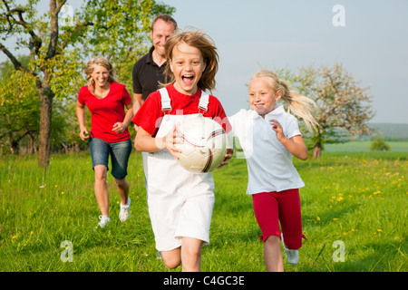 La famiglia felice giocando a calcio, un bambino ha agguantato la sfera ed è inseguito da altri Foto Stock
