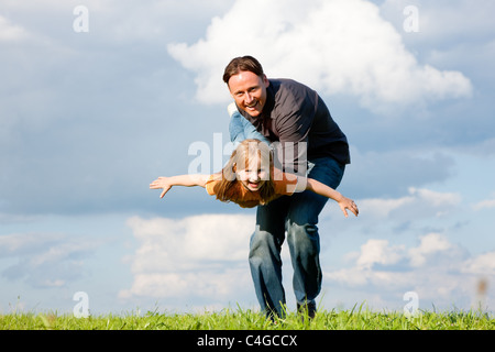 Il padre e il figlio - figlia - giocando insieme a un prato, sta portando il suo sulle mani Foto Stock