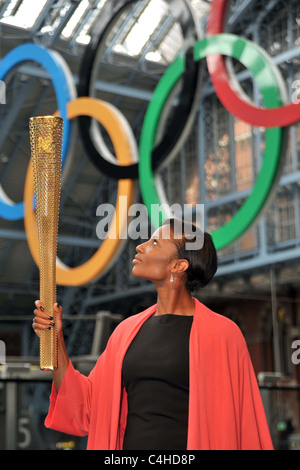 Denise Lewis guarda fino alla torcia come egli lo tiene sotto gli anelli olimpici. 2012 Londra Torcia olimpica Foto Stock