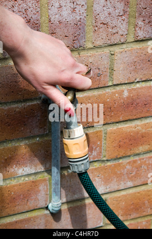 Close up di giovani caucasici mano womans ruotando il rubinetto esterno su un muro di mattoni sulla giornata di sole Foto Stock