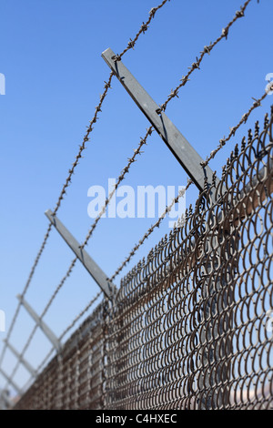 L'immagine verticale di una maglia di catena di recinzione di sicurezza e rabboccato con tre trefoli di filo spinato Foto Stock