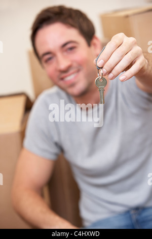 Giovane uomo si siede sul pavimento intorno a scatole tenendo la chiave in mano Foto Stock