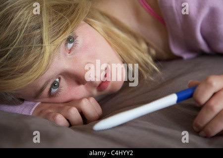 Premuto ragazza adolescente seduto in camera da letto con test di gravidanza Foto Stock