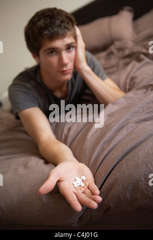 Premuto ragazzo adolescente seduto in camera da letto con le Pillole Foto Stock