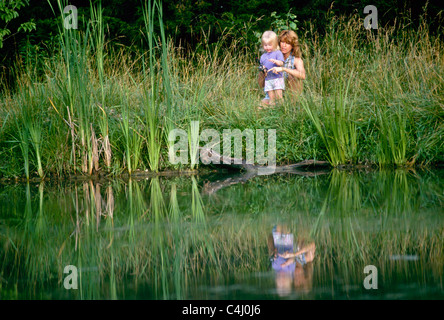 Madre insegnare la sua giovane figlia di pescare nel lago rurale nel mezzo di erba alta sulla riva, Missouri, Stati Uniti d'America Foto Stock